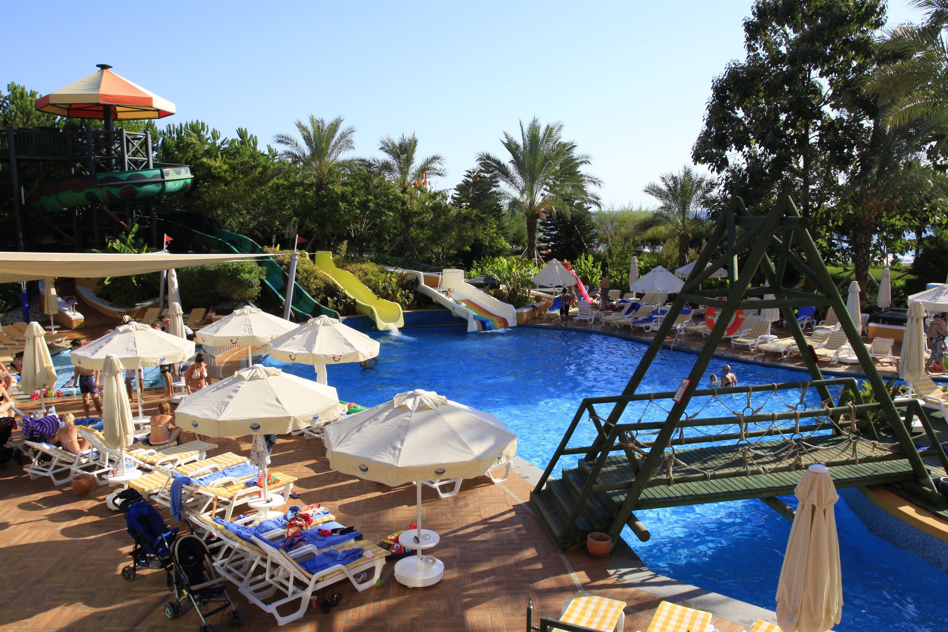Zona de piscina con toboganes, sombrillas, sillas de descanso y una pequeña estructura de juegos.