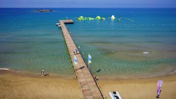 Un muelle de madera que se adentra en un mar azul y transparente, con una playa de arena al final.