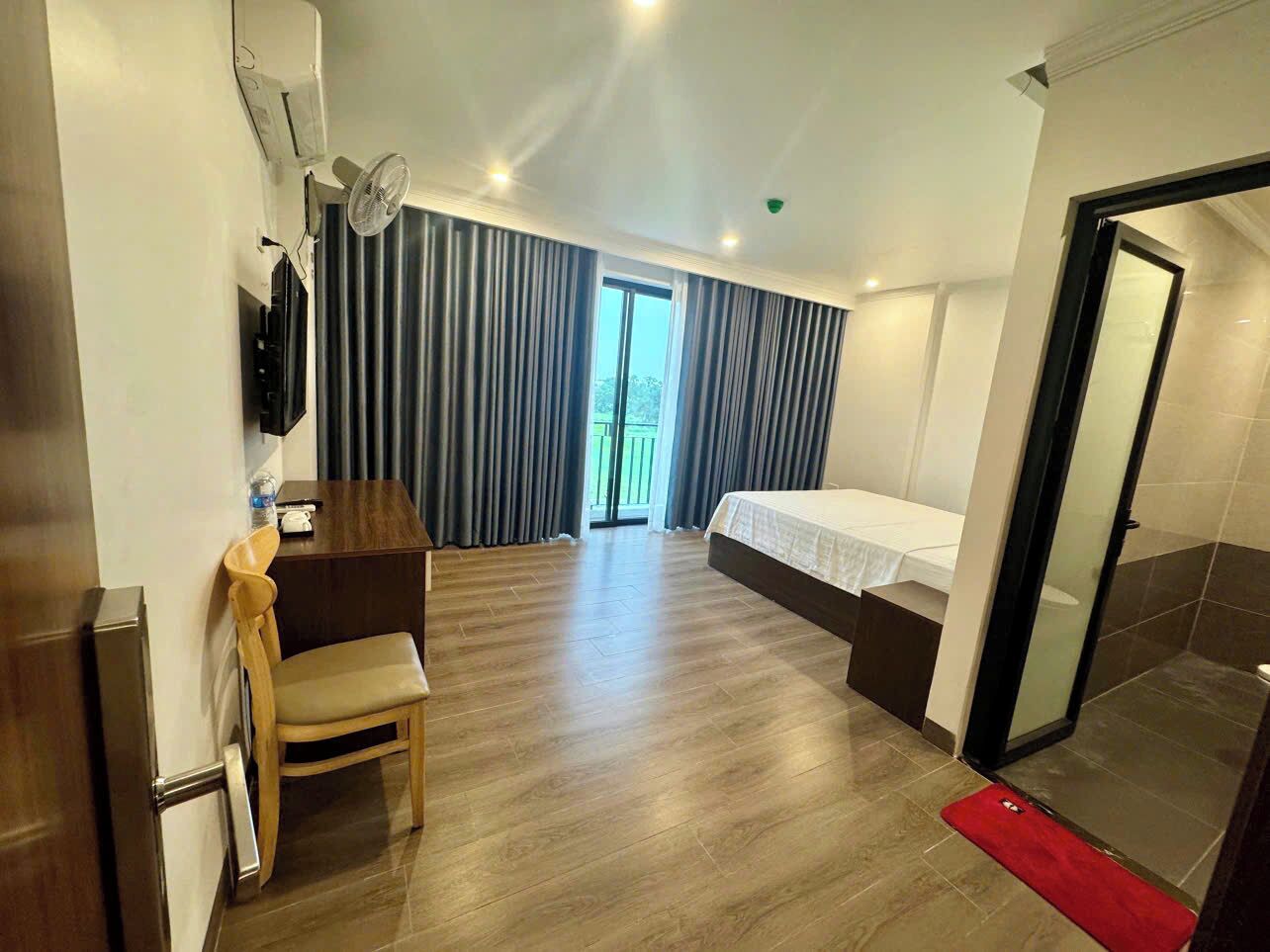 Habitación de hotel con cama, escritorio, silla, televisor y puerta corredera al baño.