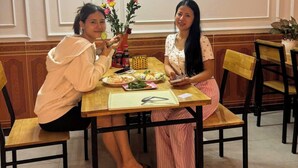Two people dining at a table with a vase of flowers, a bottle of sauce, and a menu. - Family Transit Hotel (Hanoi)