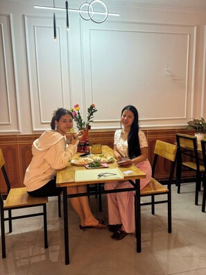 Two people dining at a table with a vase of flowers, a bottle of sauce, and a menu. - Family Transit Hotel (Hanoi)