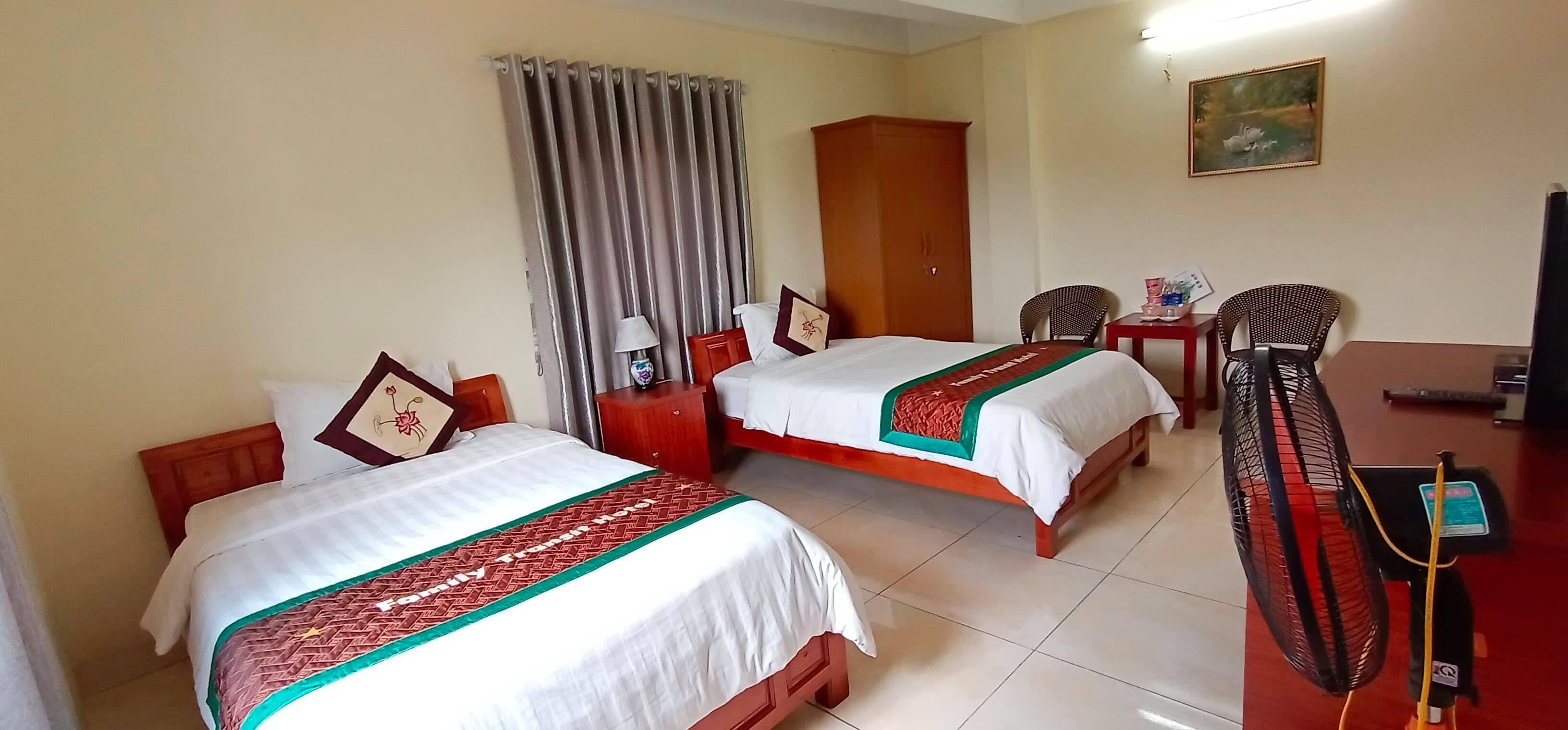 A hotel room with two beds, a wardrobe, a desk with a chair, a television, and a fan.