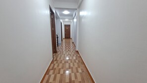 A hallway with a checkered wooden floor, white walls, and a door at the end. - Family Transit Hotel (Hanoi)