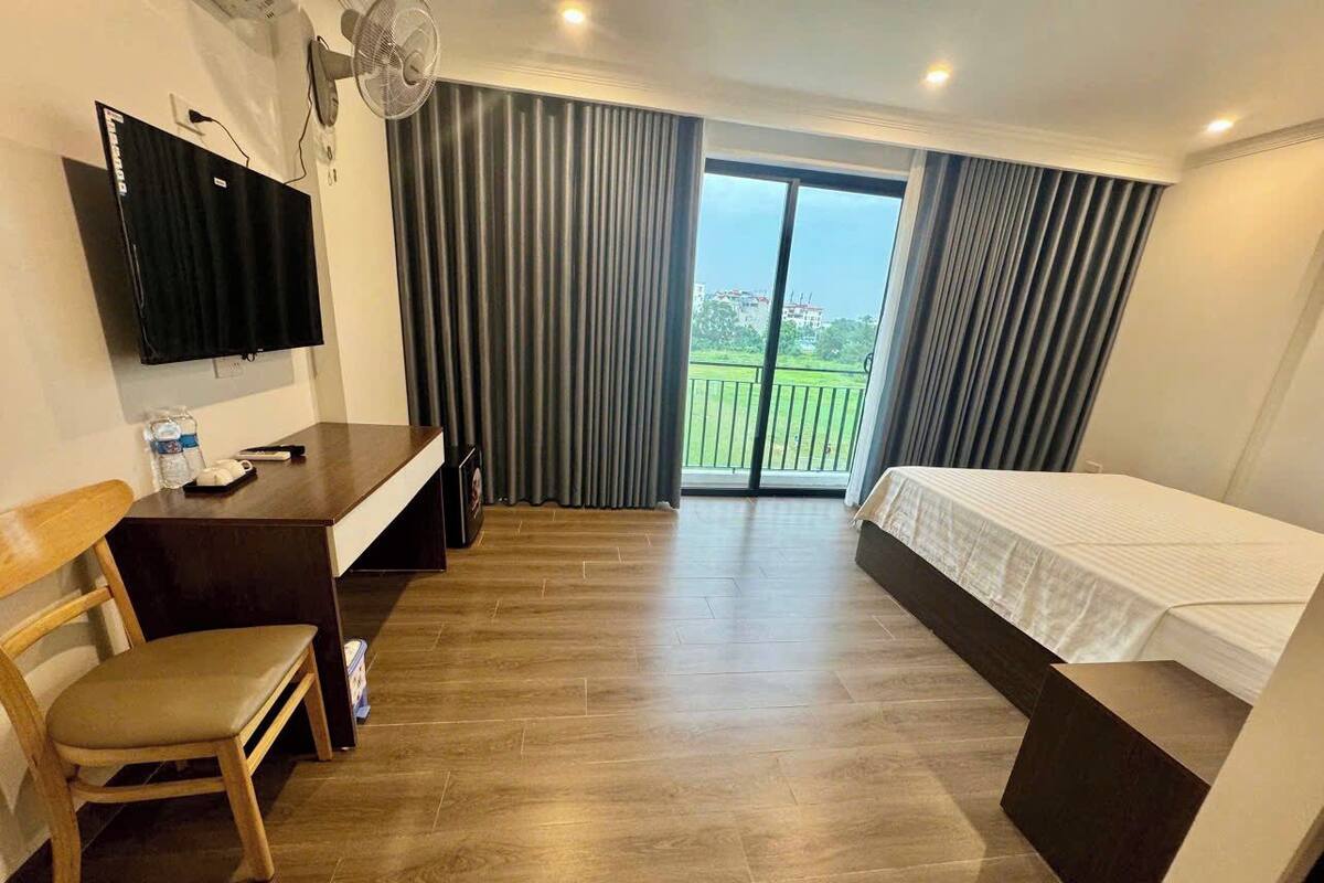 A hotel room with a bed, a desk, a chair, a TV, and a balcony with curtains.