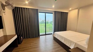 A hotel room with a bed, a TV, a fan, and a balcony with curtains. - Family Transit Hotel (Hanoi)