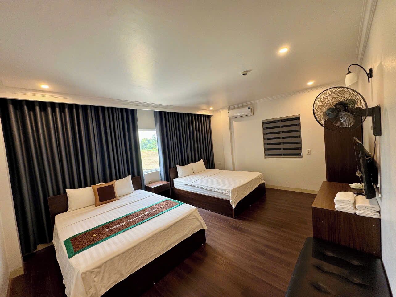 A hotel room with two beds, a desk, a fan, and a window with curtains.
