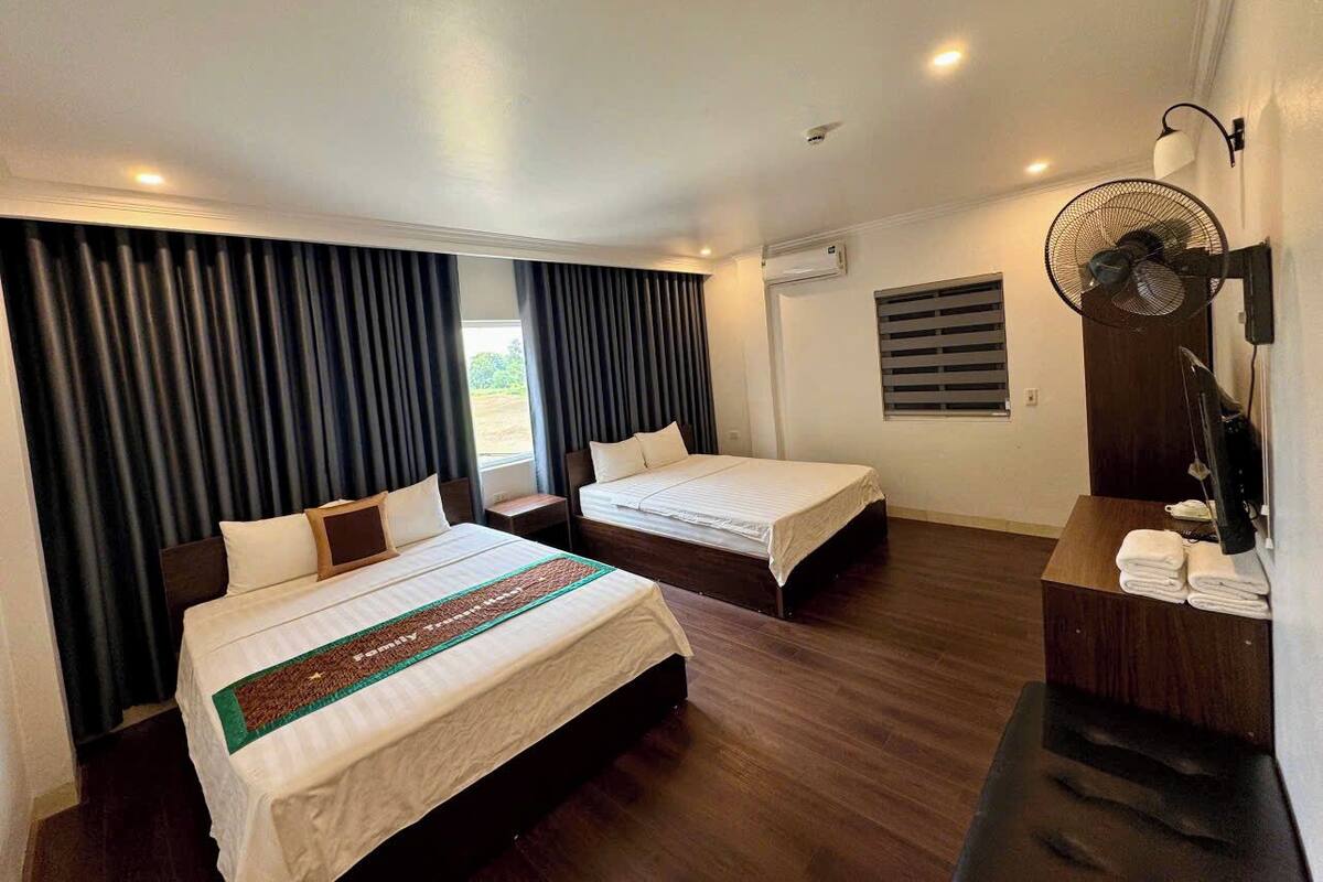 A hotel room with two beds, a desk, a fan, and a window with curtains.