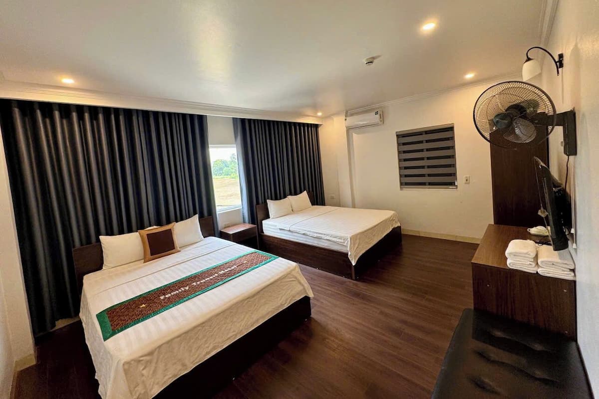 Habitación de hotel con dos camas, un escritorio, un ventilador y una ventana con cortinas.