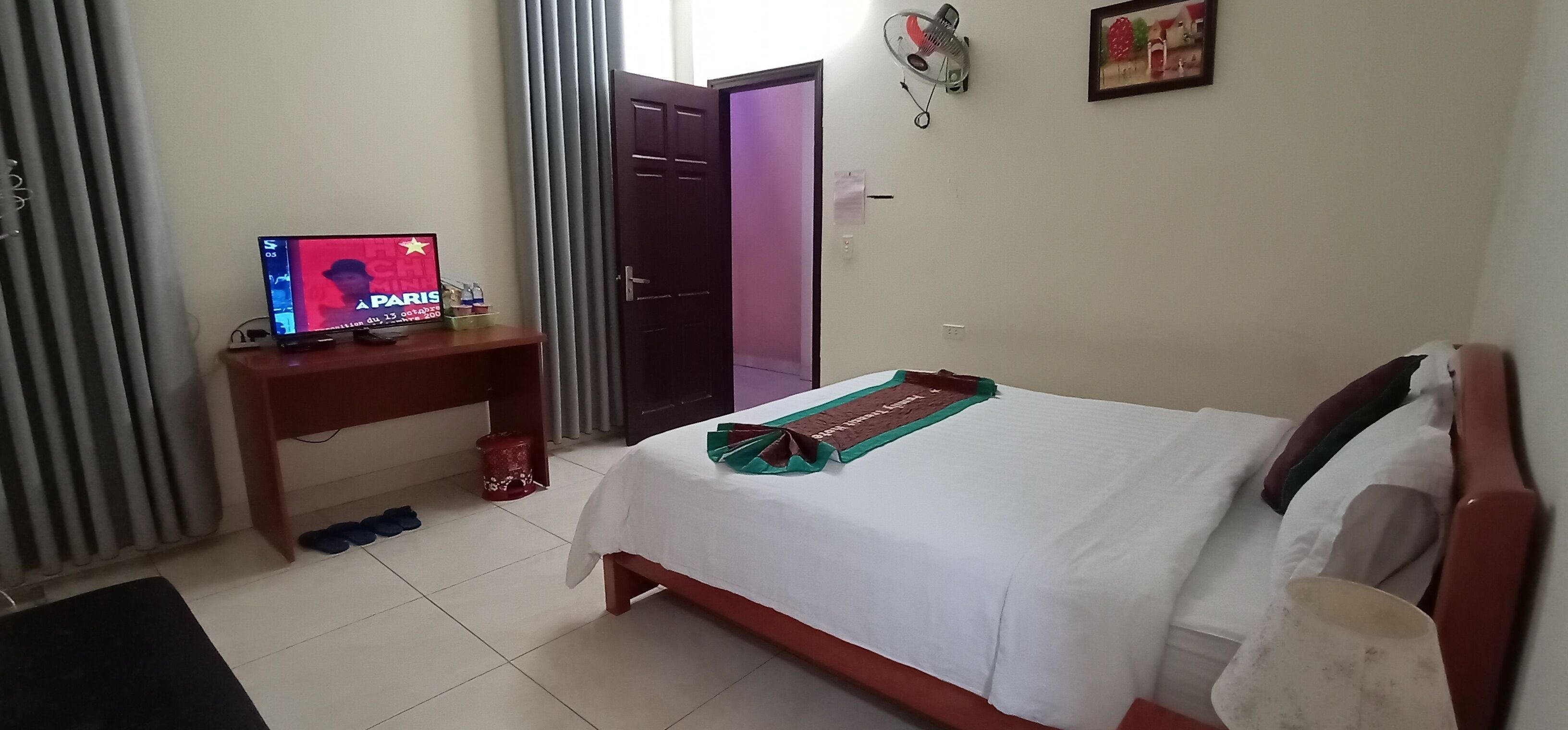Une chambre d’hôtel avec un lit, un téléviseur posé sur une table en bois, une poubelle rouge et une porte donnant sur une autre pièce.