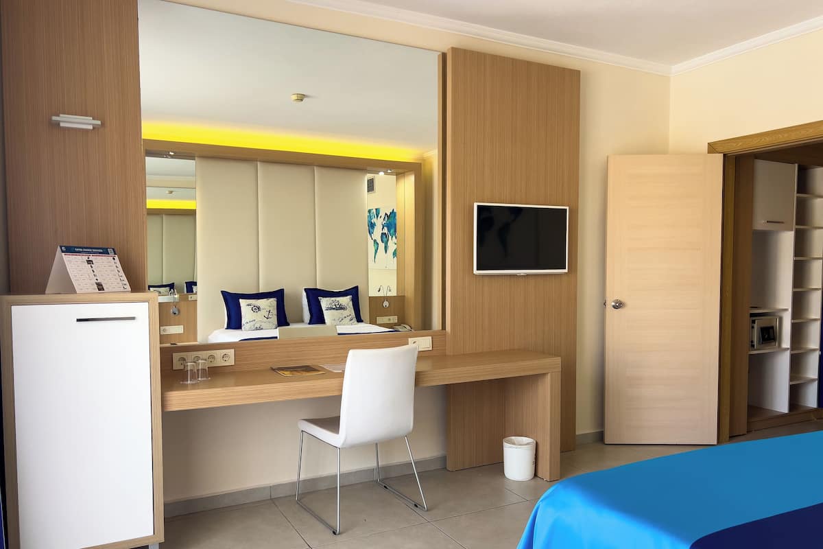 Habitación de hotel con cama, escritorio con silla, refrigerador, televisión y armario.