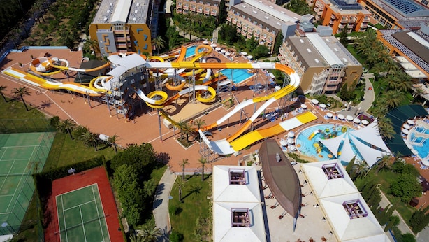 Vista aérea de un parque acuático con toboganes y piscinas, rodeado de edificios de hotel.