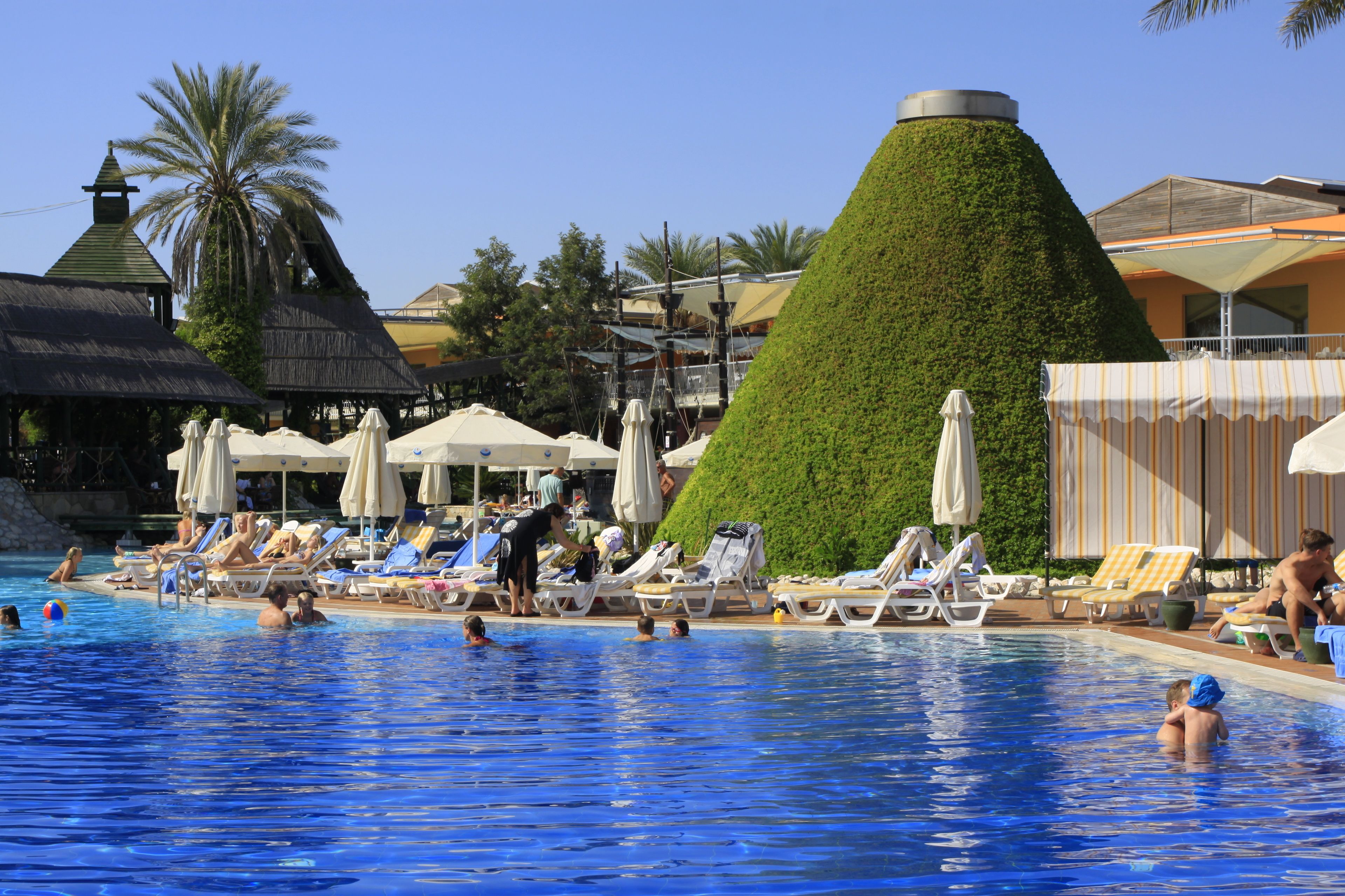 A swimming pool with lounge chairs and umbrellas, surrounded by buildings with a tropical theme.