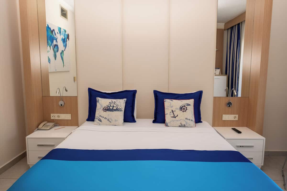 Habitación de hotel con una cama grande, dos mesitas de noche, un teléfono y un espejo en la pared.