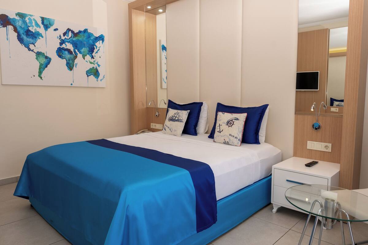 Una habitación de hotel moderna con una cama grande, una mesita de vidrio, un escritorio pequeño y un gran mapa del mundo en la pared.