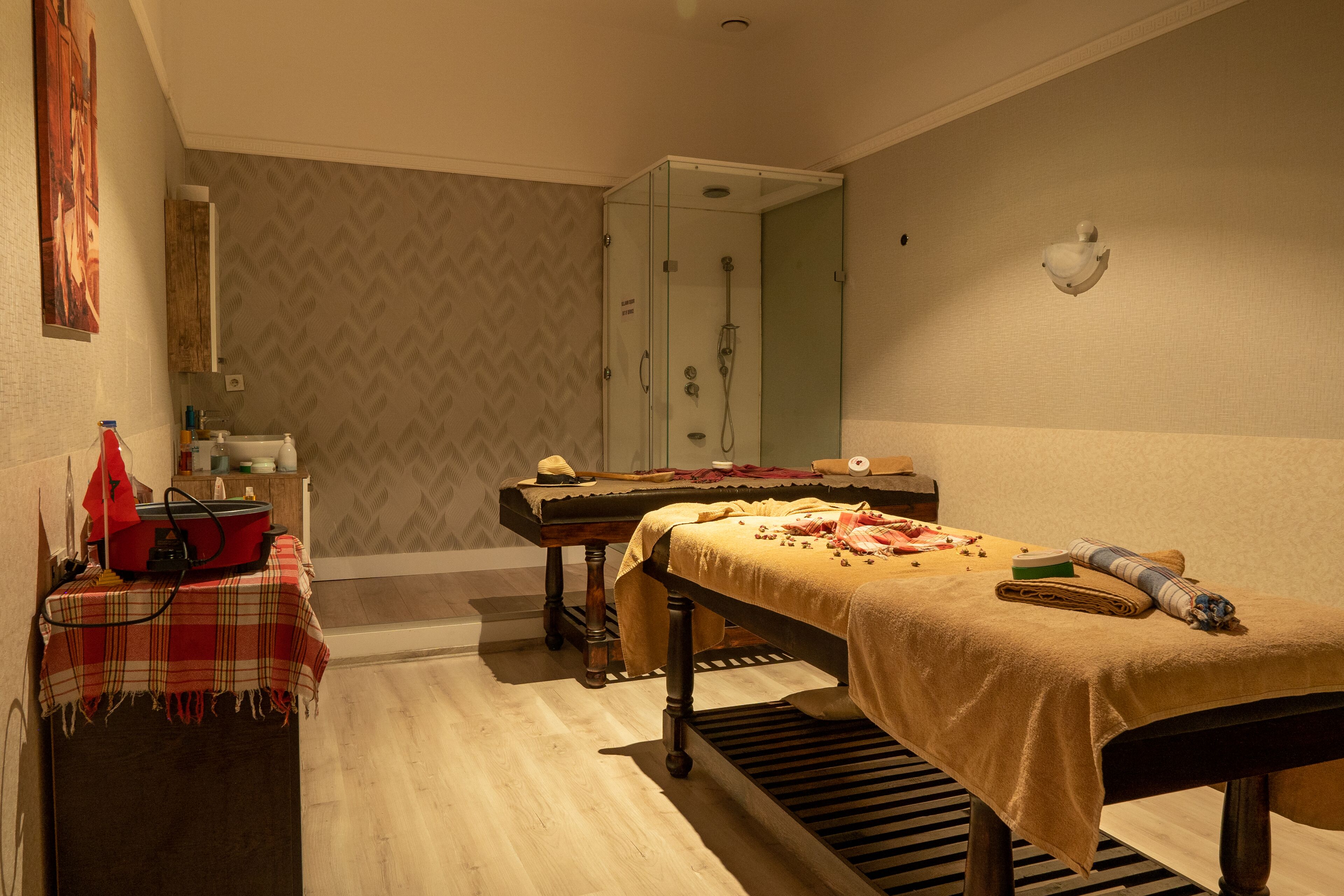 Una habitación con cama, una mesita con un objeto rojo, un espejo y un área de ducha.