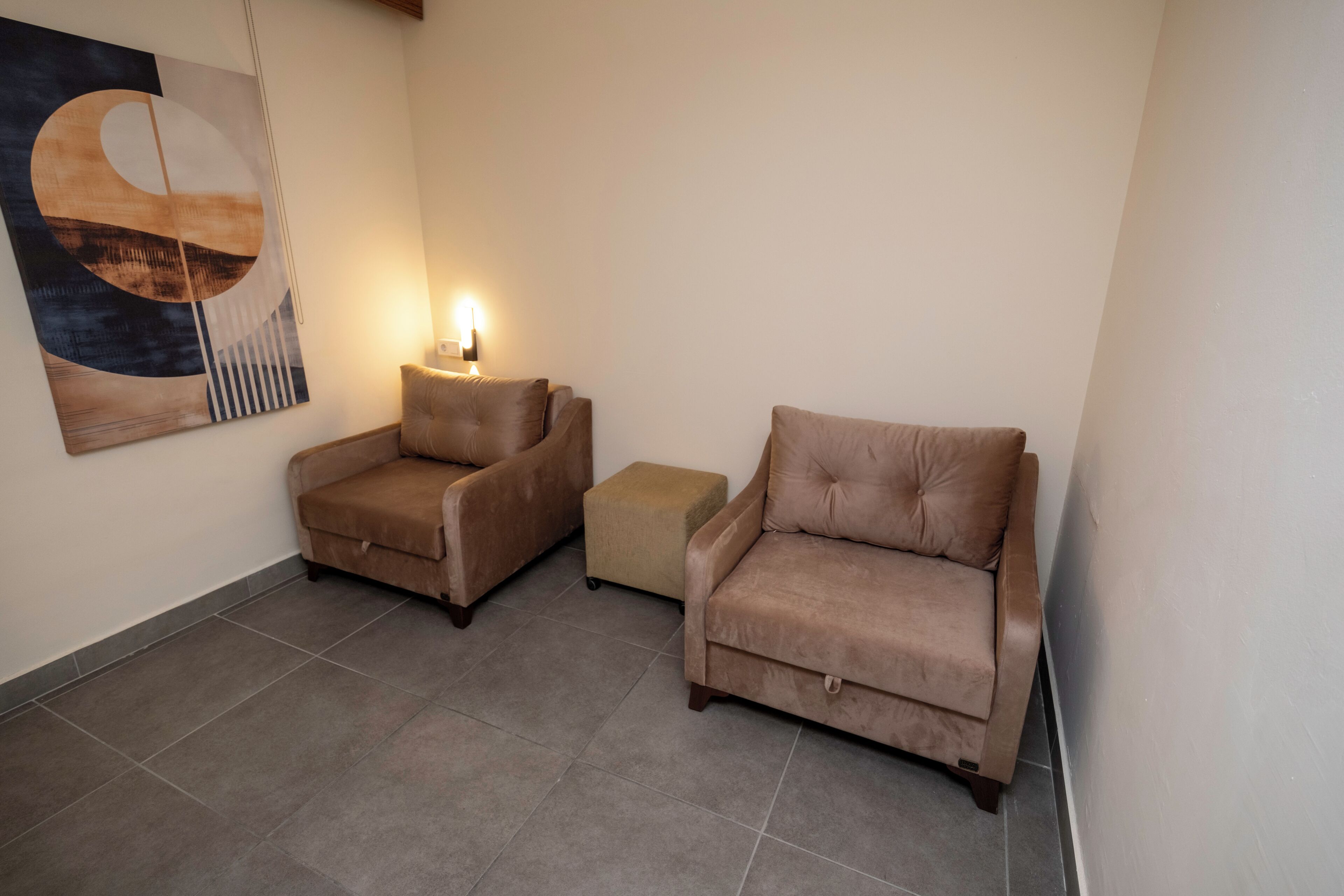 Una habitación con dos sofás, un pequeño reposapiés y una lámpara de pared.