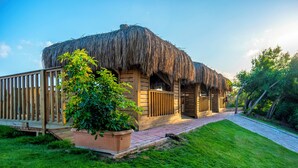 Una estructura de madera con techo de paja, una terraza de madera y un camino pavimentado.