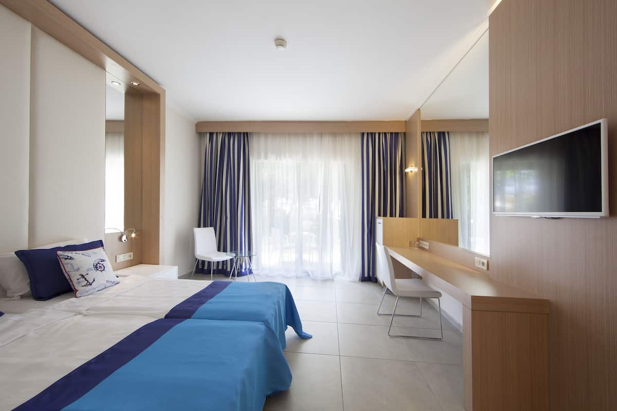 Habitación de hotel con cama, escritorio, silla, televisión y ventana con cortinas.