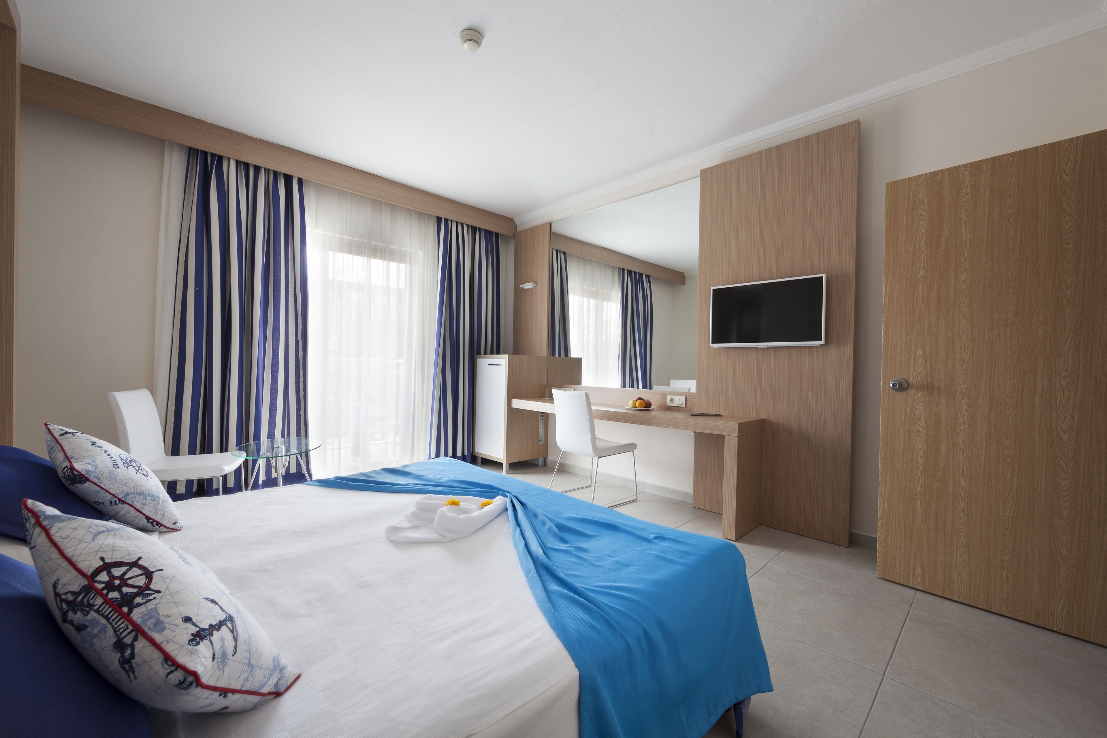 A hotel room with a bed, a desk, a chair, a TV, and a wardrobe.