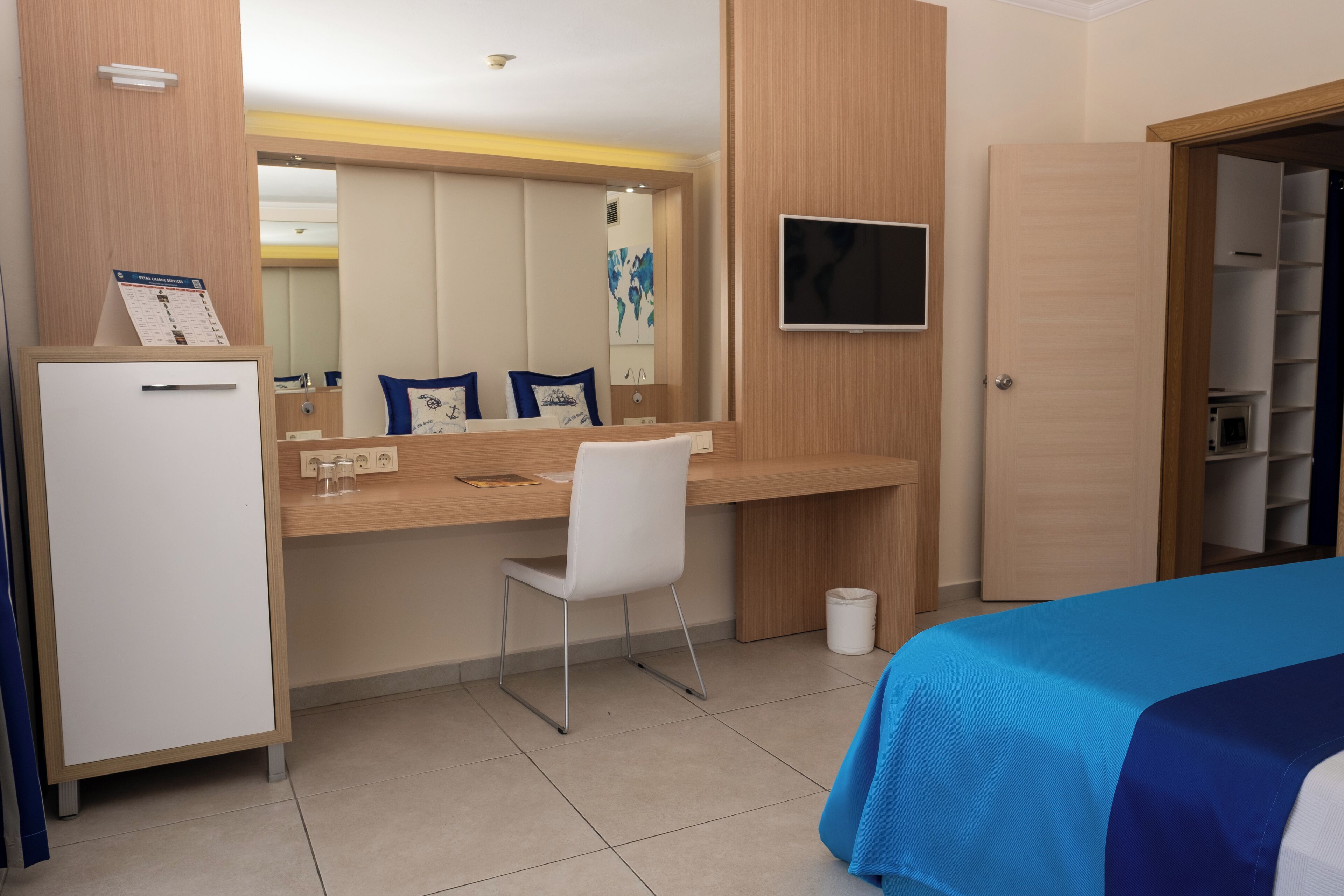 Een hotelkamer met een bed, een bureau met stoel, een televisie, een kledingkast en een kleine prullenbak.