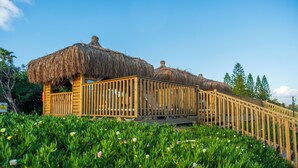 Estructura de madera con techos de paja, rodeada de abundante vegetación y flores.