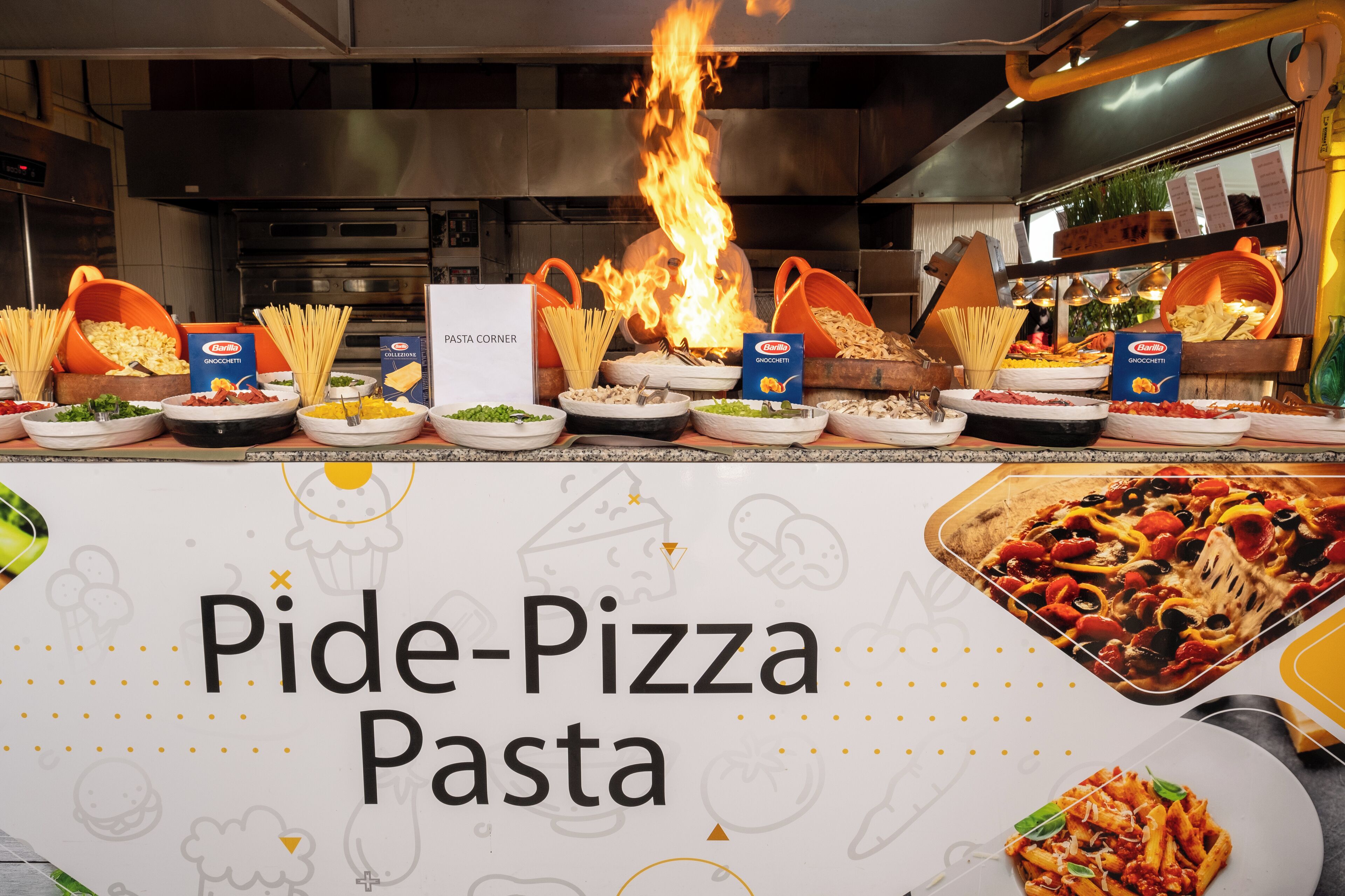A kitchen counter with various pasta dishes and a sign that reads "Pide-Pizza Pasta".
