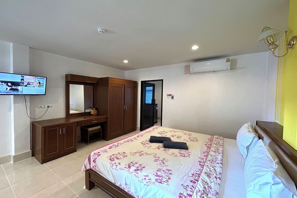 A hotel room with a bed, a TV mounted on the wall, a wardrobe, and an air conditioning unit.
