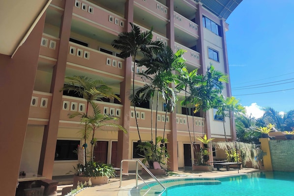 A multi-story hotel with balconies, a swimming pool, and tropical plants.