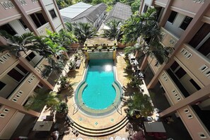 A multi-level building with a central swimming pool surrounded by palm trees and potted plants. - SB Park Mansion (Wichit)
