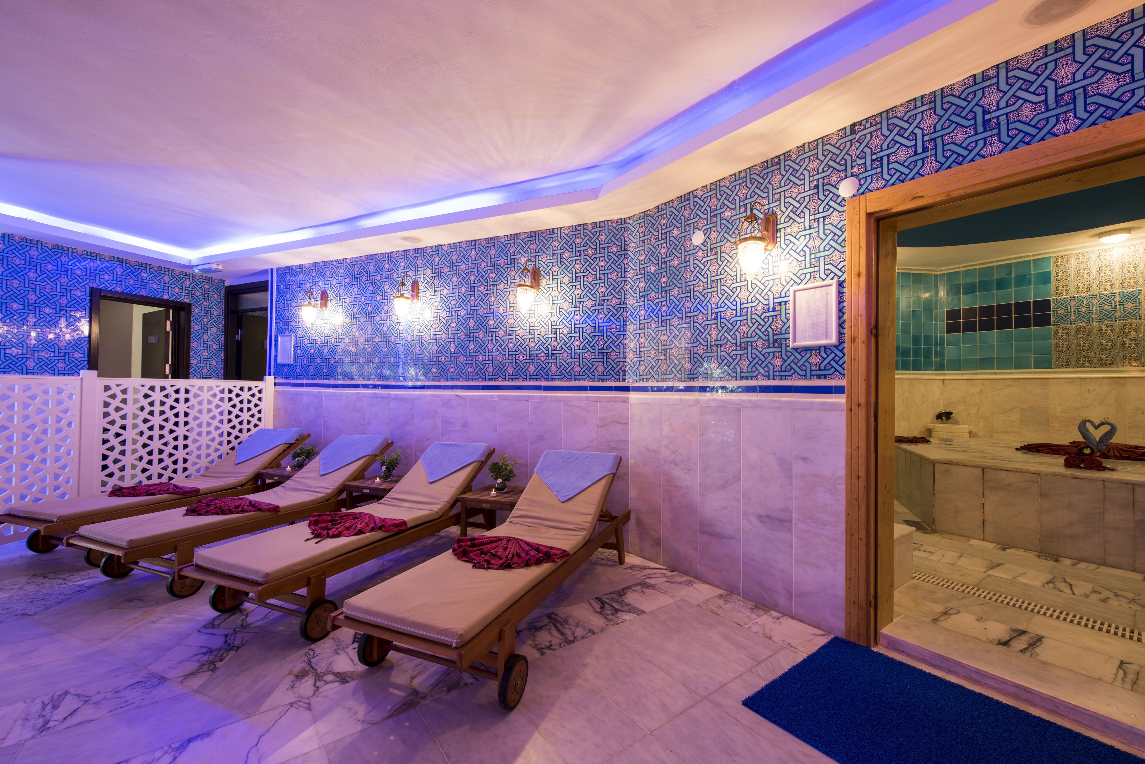 A spa area with multiple sun loungers, a wooden reception desk, and a tiled wall with a geometric pattern.