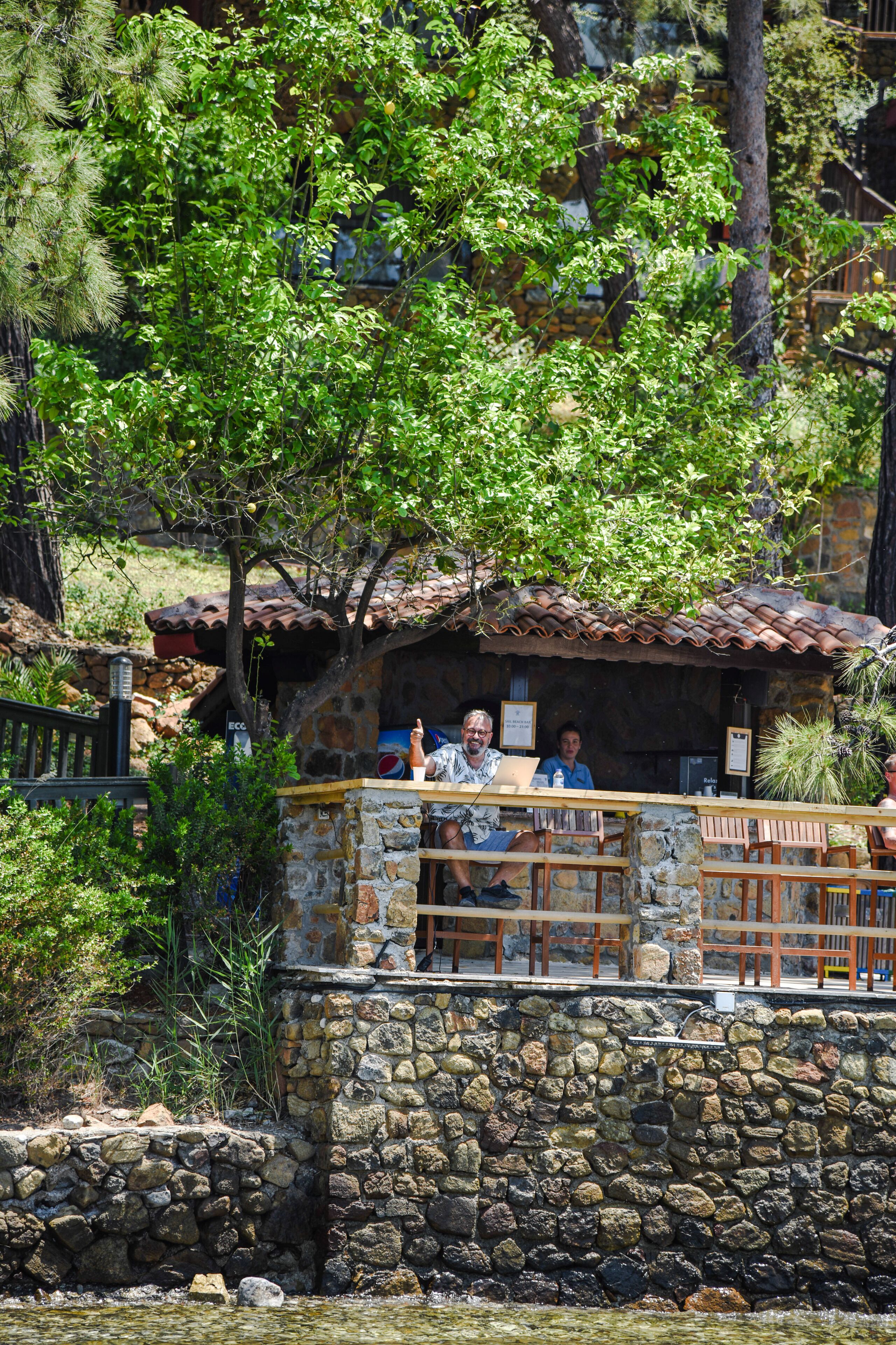 A stone building with a tiled roof, surrounded by greenery and a stone wall.