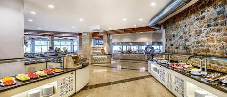 A buffet area with various food stations, a stone wall, and a kitchen in the background.