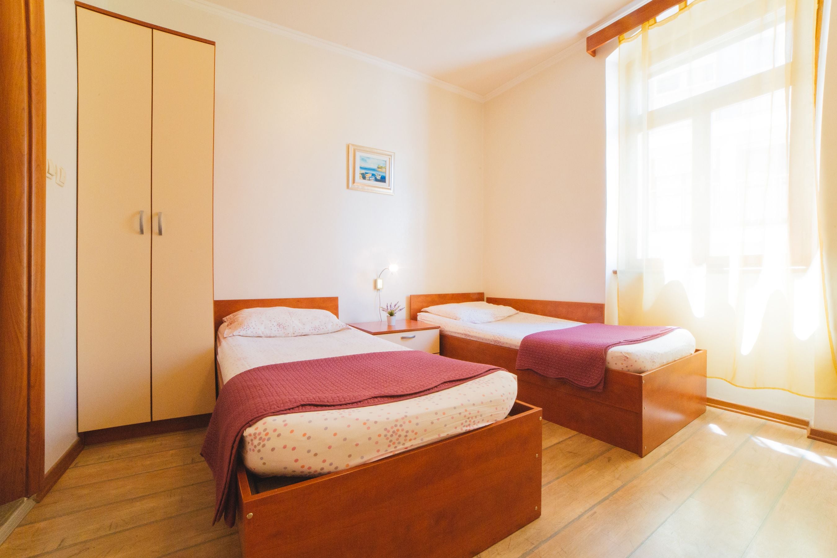 Een slaapkamer met twee bedden, een garderobe, een nachtkastje met een lamp en een raam met gordijnen.