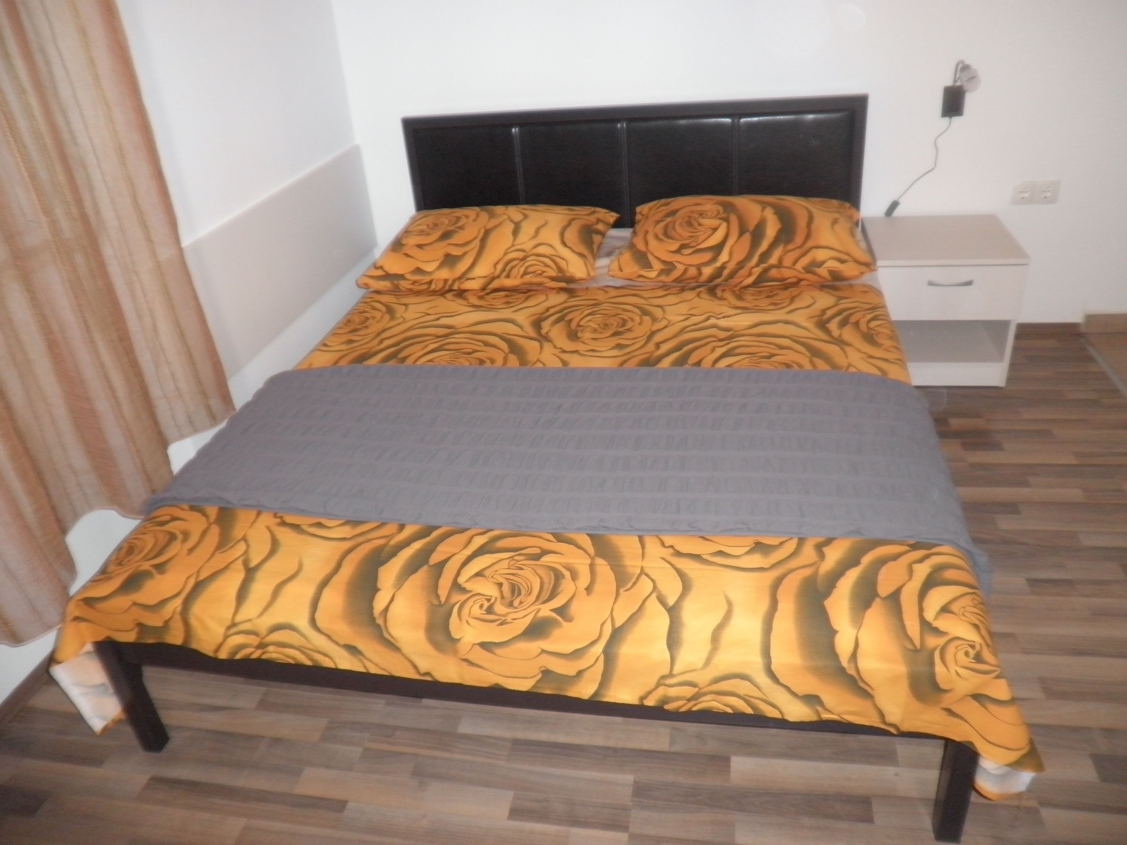 A bed with a floral bedspread, a grey blanket, and a wooden headboard.