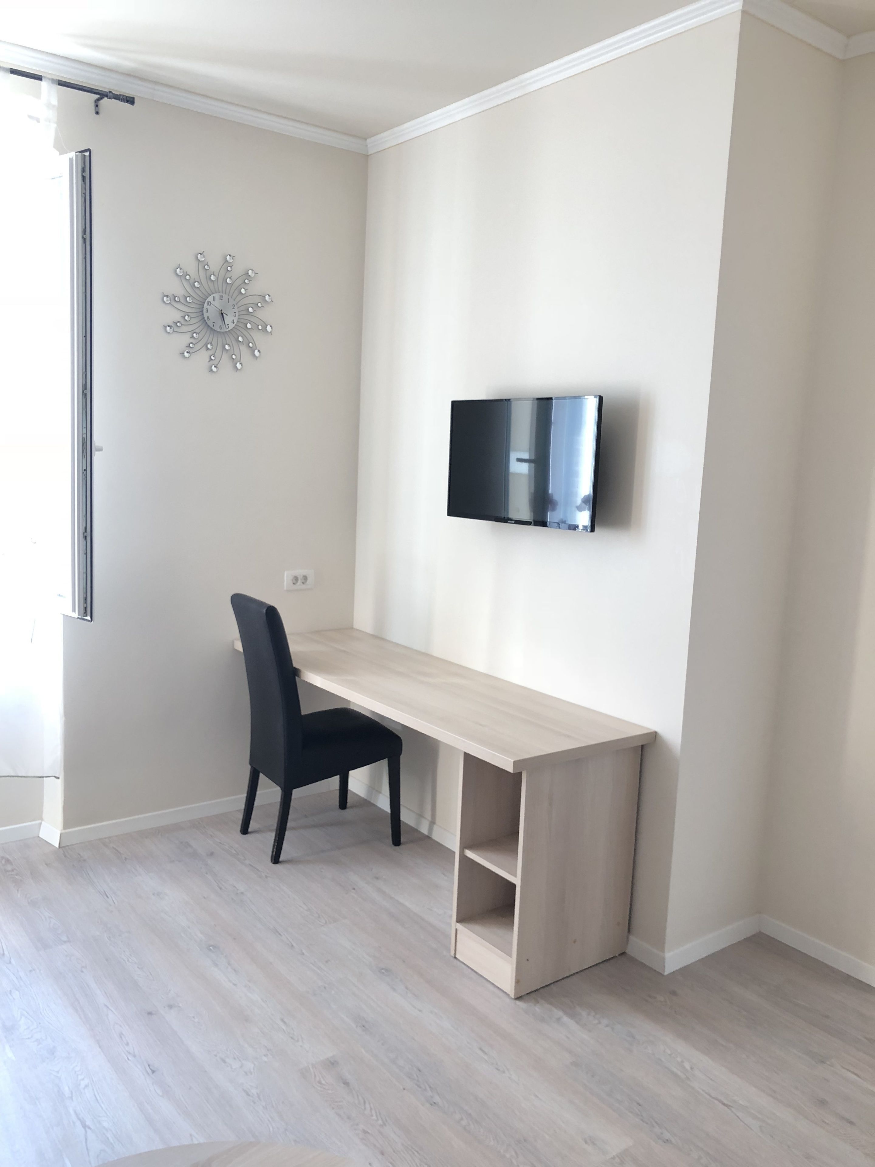 Quarto de canto com escrivaninha de madeira, uma cadeira preta, televisão montada e um detalhe decorativo na parede.