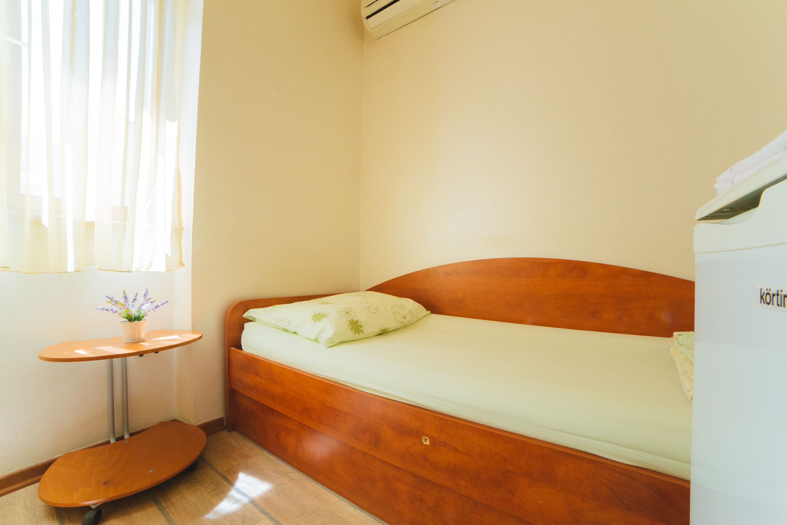 A small, cozy room with a wooden bed, a small table, and a potted plant by the window.