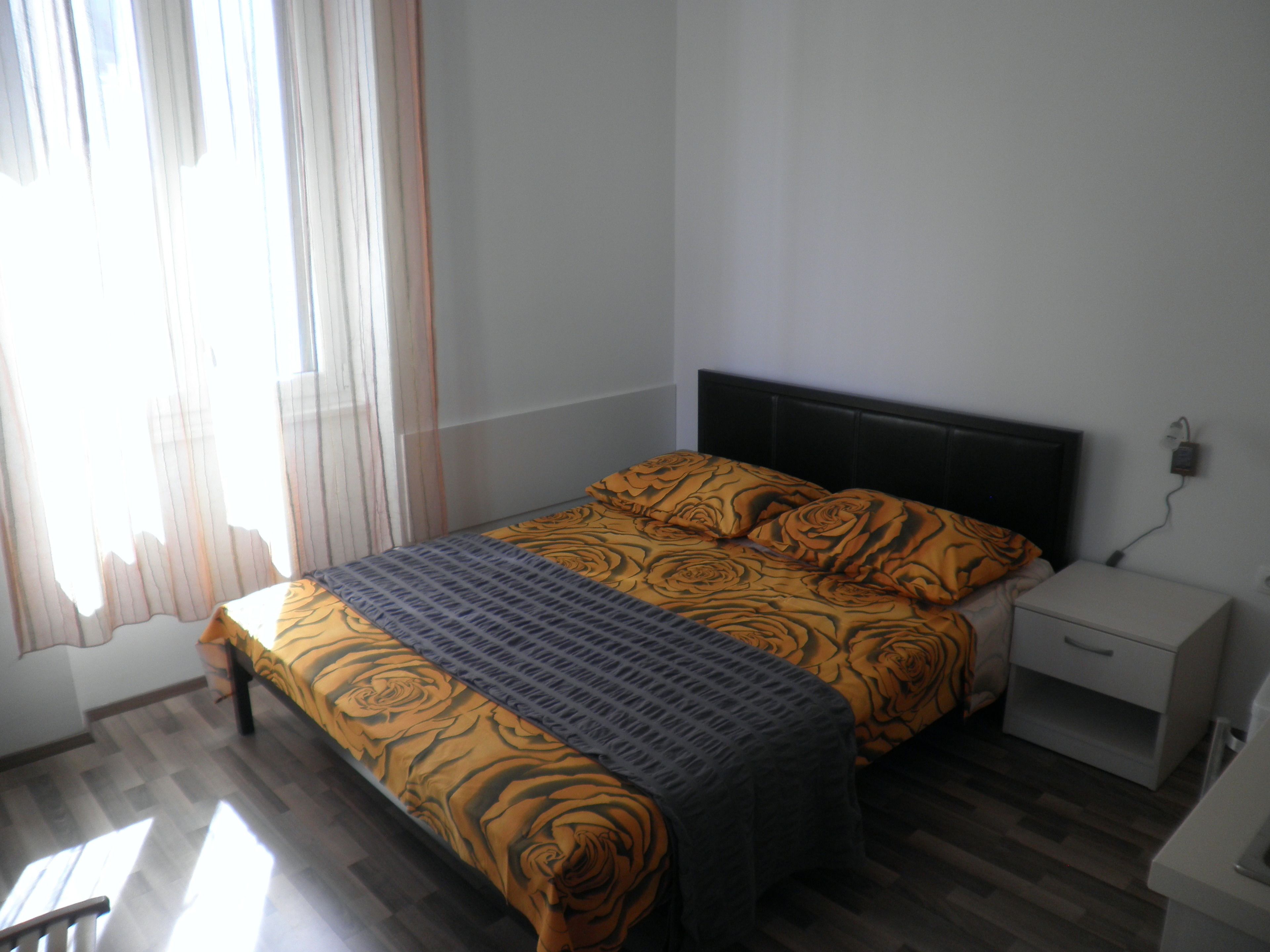 Un dormitorio con una cama, una mesita de noche y un ventanal con cortinas.