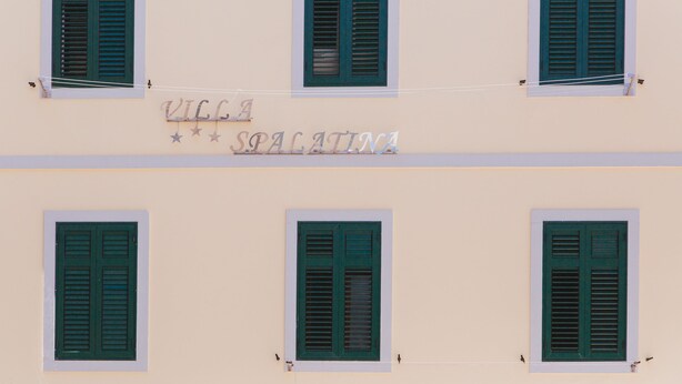 A building facade with four windows, each featuring green shutters.