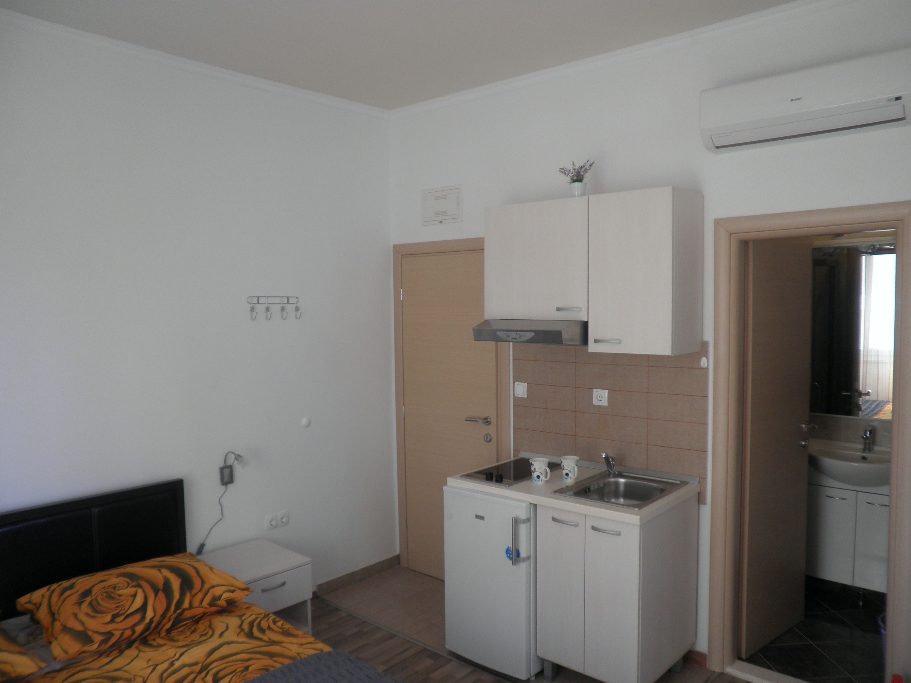 A compact room with a bed, a small kitchenette, a bathroom, and a door leading to another room.