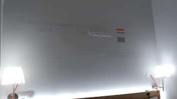 Habitación de hotel con una cama, dos lámparas de noche y una pared con una cita motivacional en español.