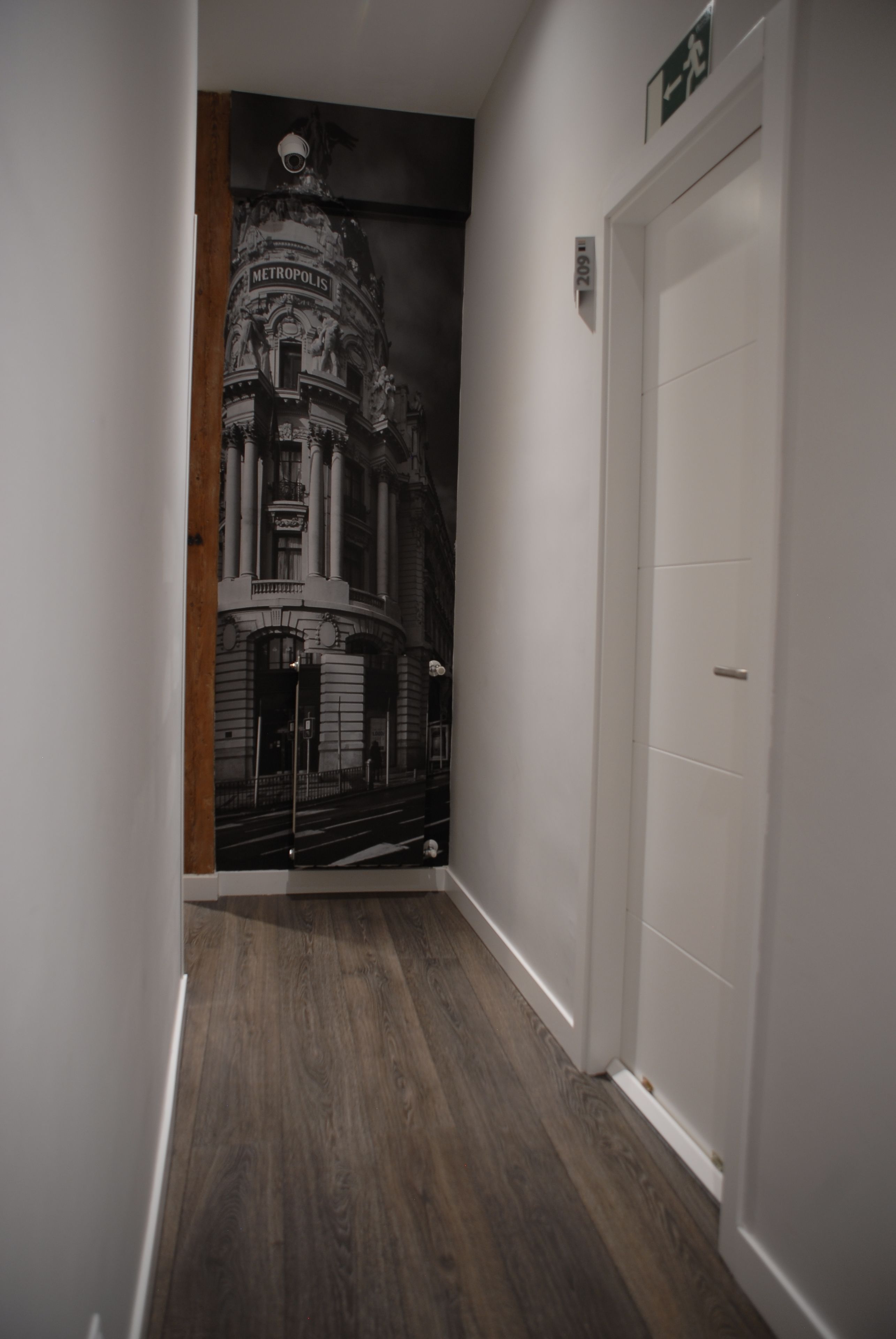 Un pasillo con un mural de un edificio clásico, una puerta blanca y suelo de madera.