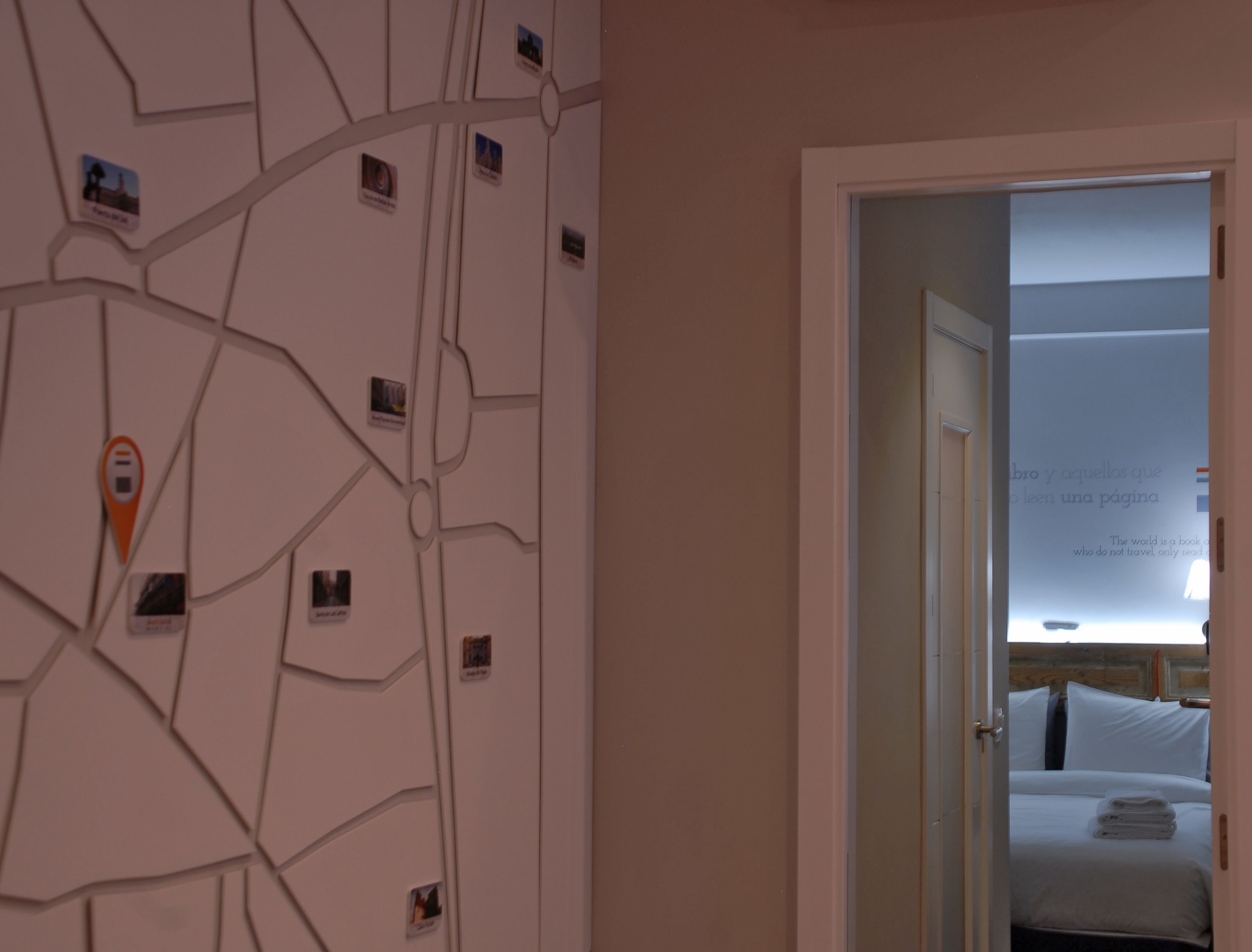 A hotel room with a map wall, a bed with white linens, and a door leading to another room.