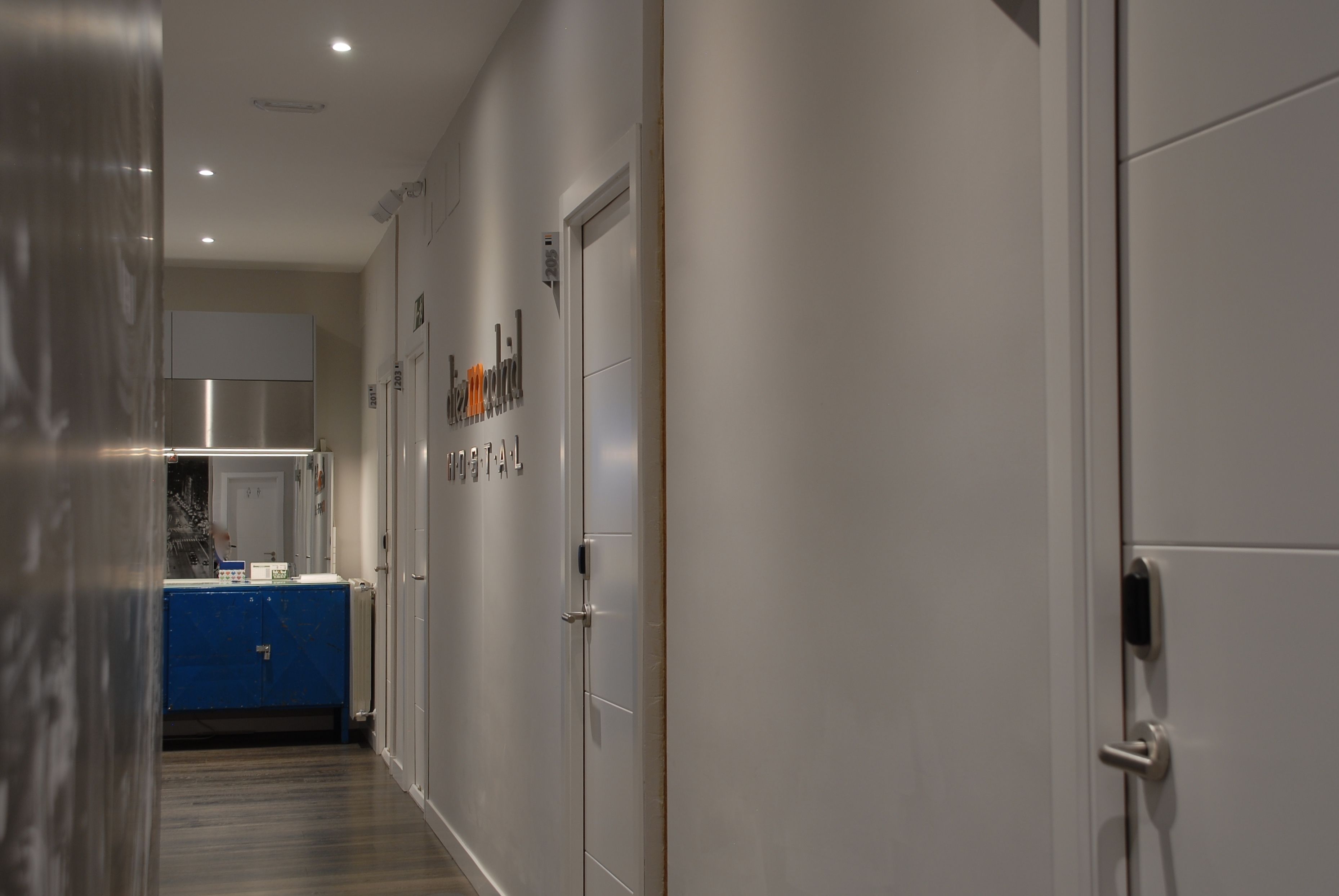 Un pasillo con un armario azul, un refrigerador de acero inoxidable y una puerta con la etiqueta 'Hospital'.