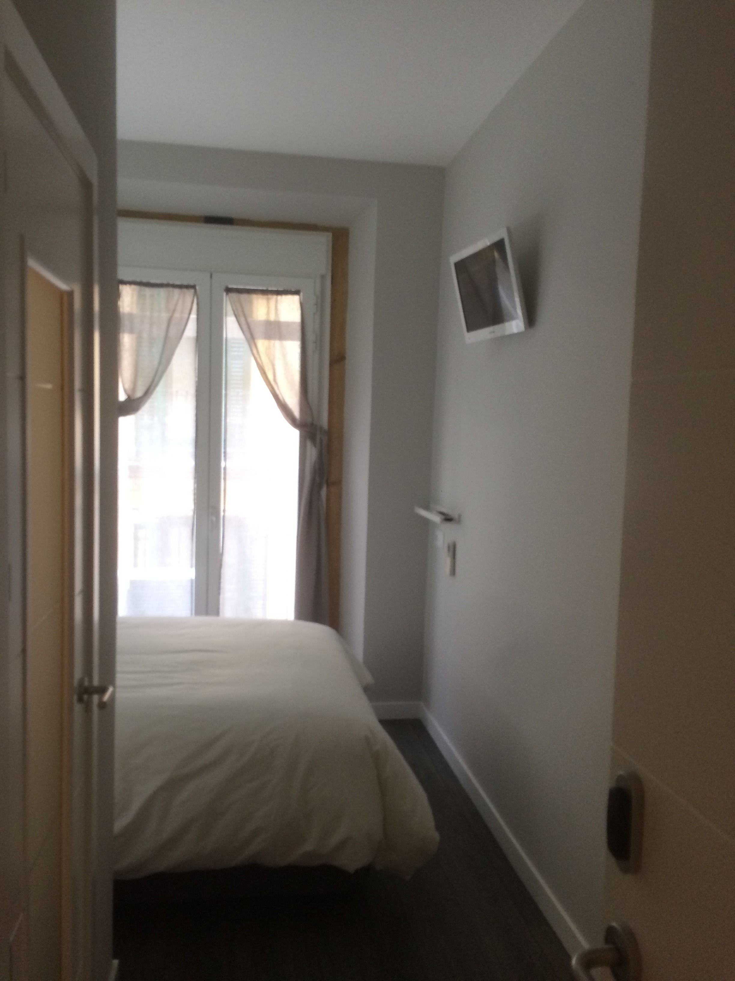 Un dormitorio con cama, televisor en la pared y puerta que da a otra habitación.
