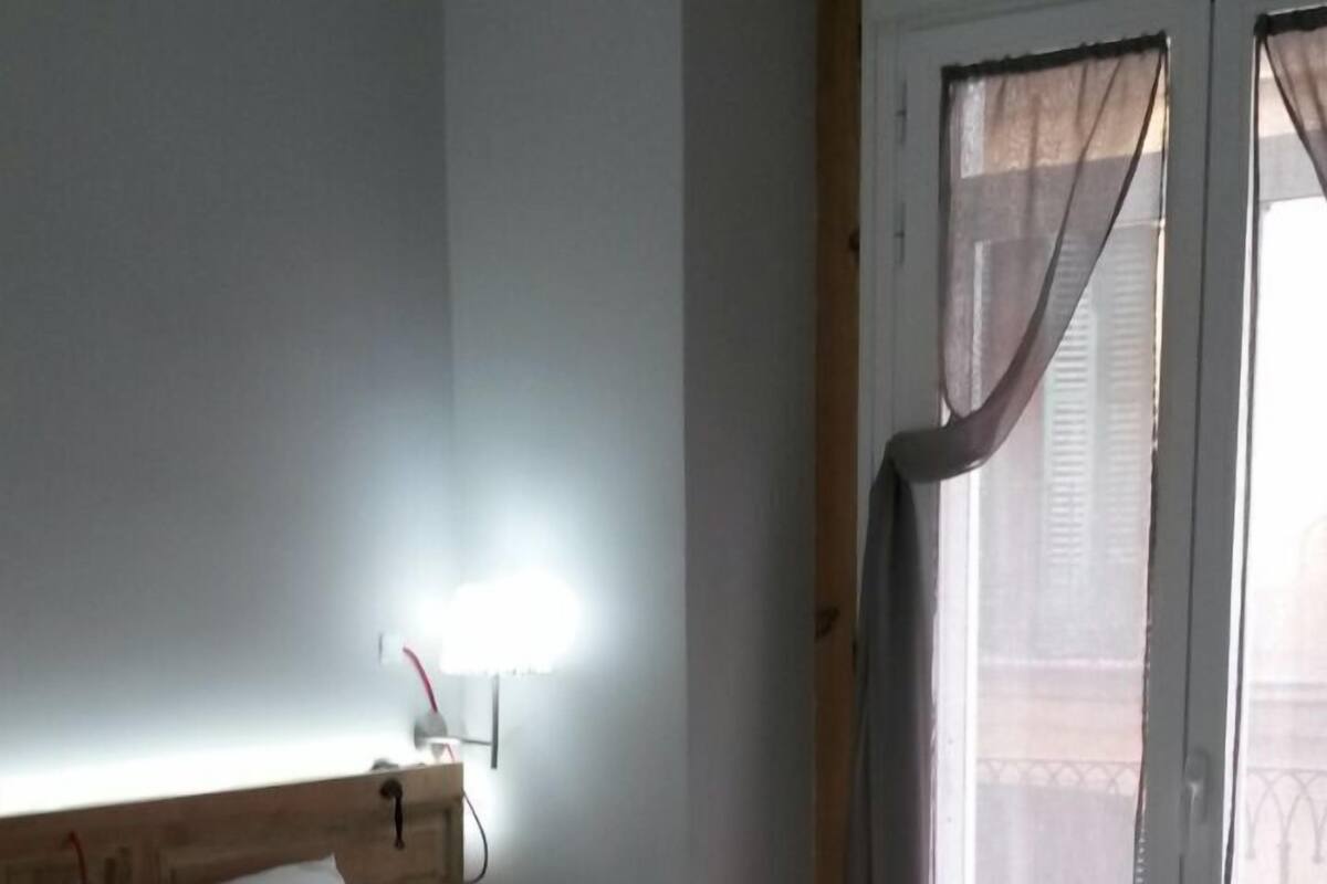 Una camera d'albergo con un letto, un comodino, una lampada e una finestra con tende.