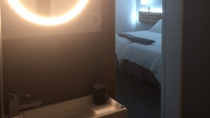 Un bagno con uno specchio rotondo, un lavandino e un piccolo cestino.