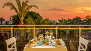A dining table set for two with a sunset view, surrounded by chairs, and palm trees in the background. - Asteria Family Resort Belek (Ex. Aquaworld Belek) - All inclusive (Serik)