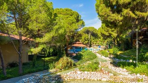 A serene garden with a clear stream, lush greenery, and a building with a red roof. - Asteria Family Resort Belek (Ex. Aquaworld Belek) - All inclusive (Serik)