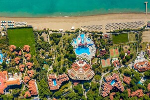Luchtbeeld van een resort met diverse zwembaden, een strand en verschillende villa's.