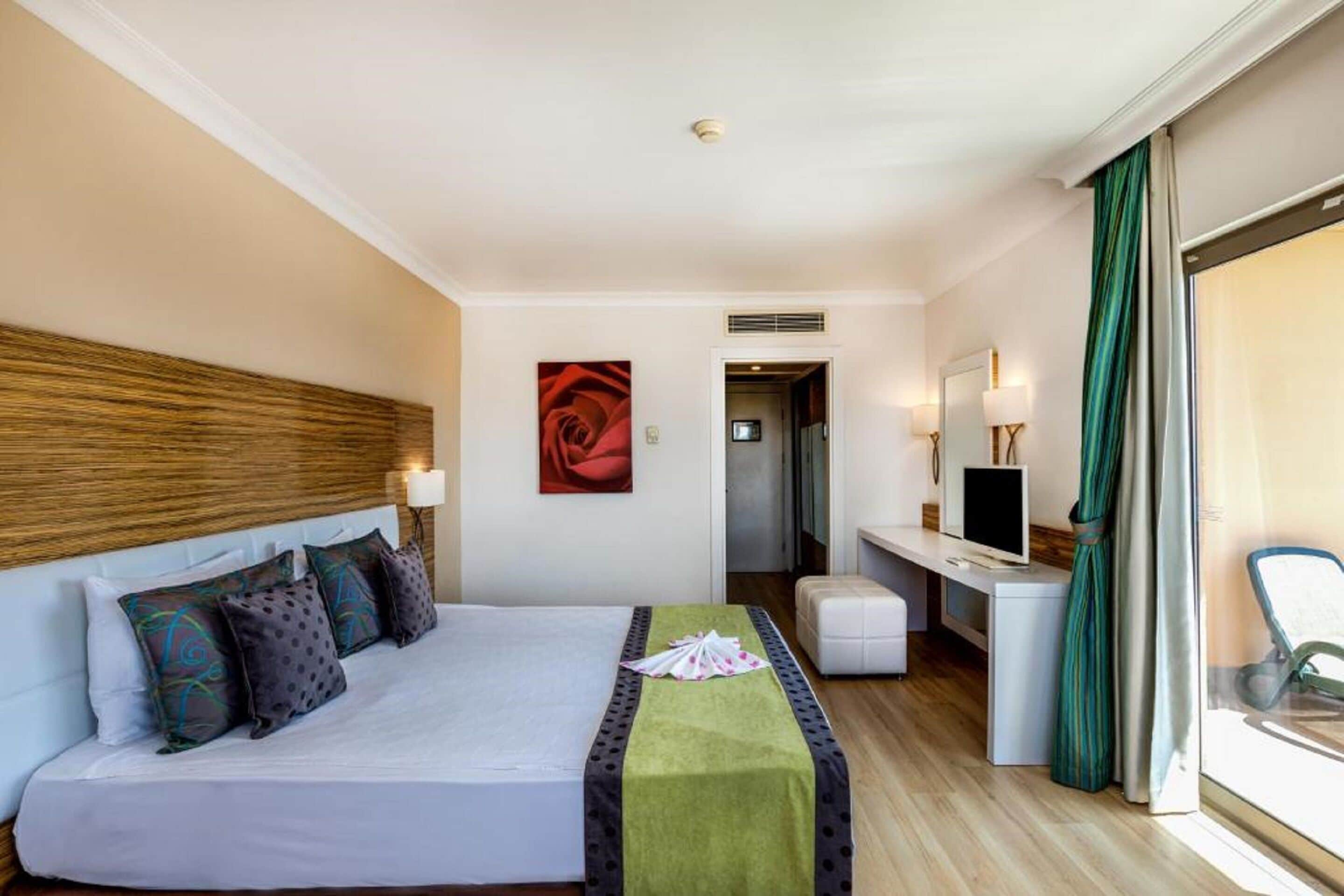 Habitación de hotel con cama, escritorio, silla, televisión y ventana con cortinas.